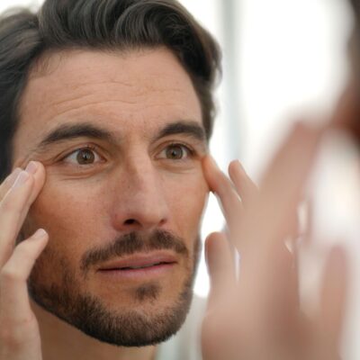 Handsome man checking wrinkles in mirror at home