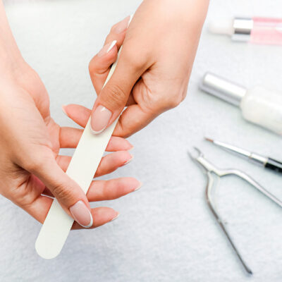 Woman holding nails file in her fingers. Manicure items like brush lacquer, nail varnish remover, scissors in background.