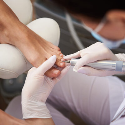 Top view picture of female specialist in sterile gloves carefully removing cuticle with special electric device